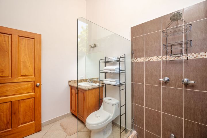 Bathroom with glass shower, wooden door, toilet, sink, and towel rack.