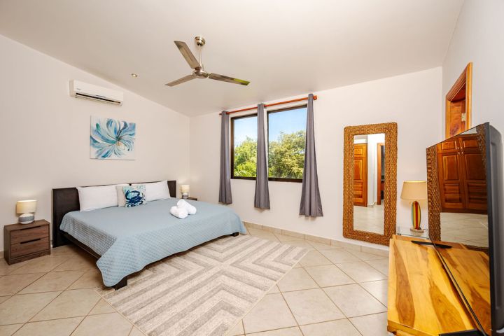 Bedroom with a large bed, window, mirror, wooden furniture, ceiling fan, and decorative painting.