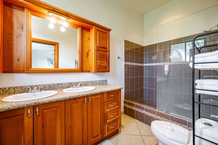 Bathroom with wooden cabinets, double sinks, large mirror, and glass shower.