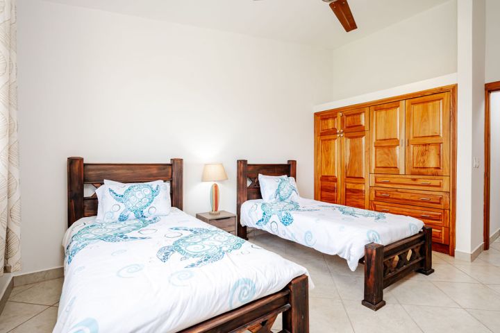 Two twin beds with turtle-themed bedding, wooden wardrobe, and nightstand in a bright room.