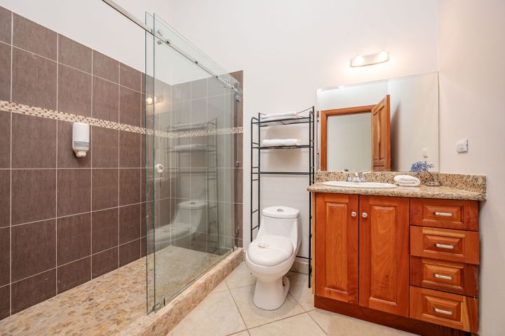 Bathroom with wooden vanity, glass shower, tiled walls, and black towel rack.