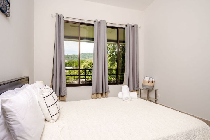 Bedroom with white bedspread, gray curtains, and window view of greenery.