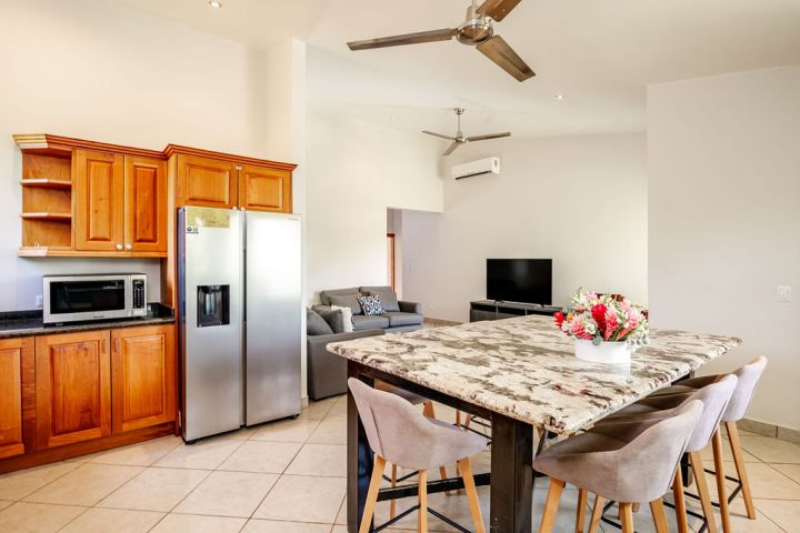 Modern kitchen and living area with wooden cabinets, marble table, and gray sofas.