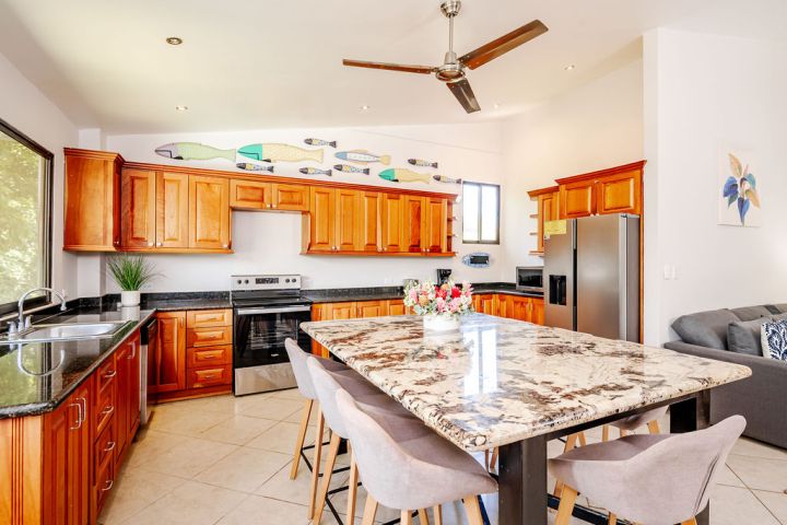 Modern kitchen with wooden cabinets, granite island, chairs, and ceiling fan.