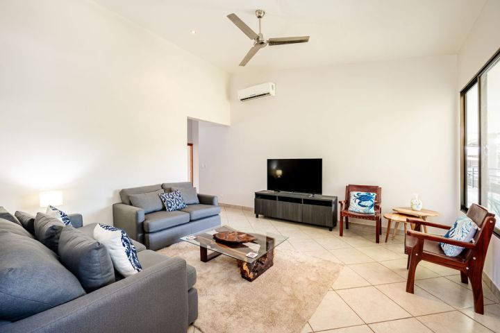 Modern living room with grey sofas, TV, wooden chairs, coffee table, and ceiling fan.