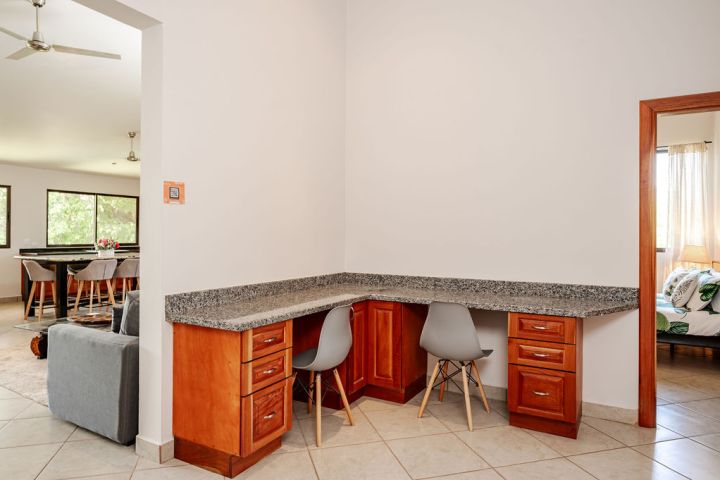 Corner desk with gray chair in a room with wooden cabinets and granite countertop.