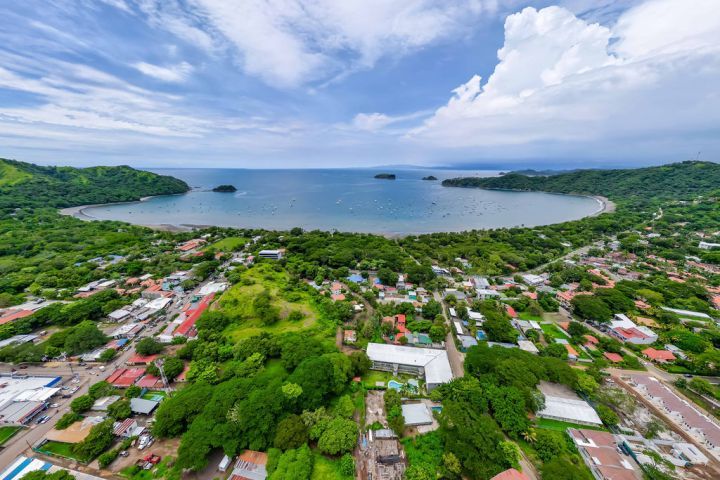 Aerial view of a coastal town with lush greenery and a curved bay with many boats.