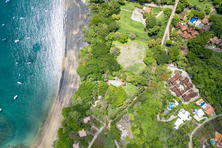 Aerial view of a coastal area with beach, ocean, trees, and houses.