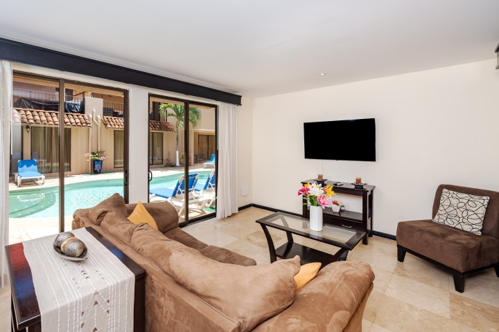 Living room with brown sofa, glass table, and pool view through sliding doors.