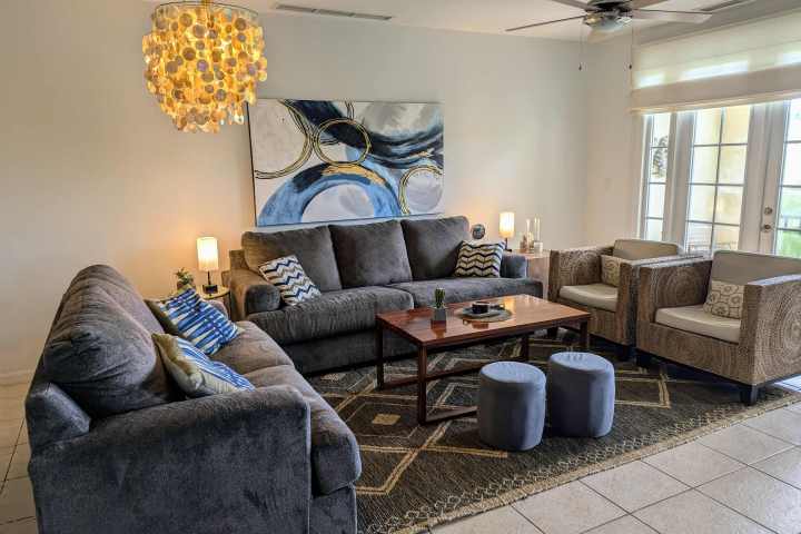 Living room with gray sofas, abstract art, chandelier, coffee table, and large windows.