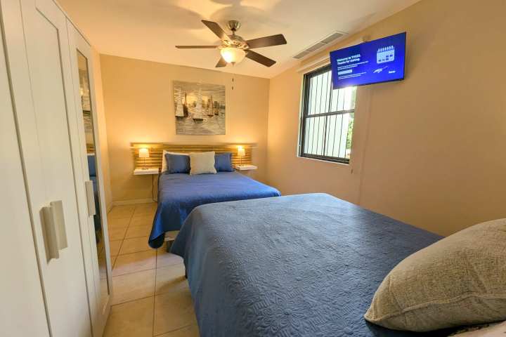 Bedroom with two beds, blue bedding, ceiling fan, wall art, and wall-mounted TV.
