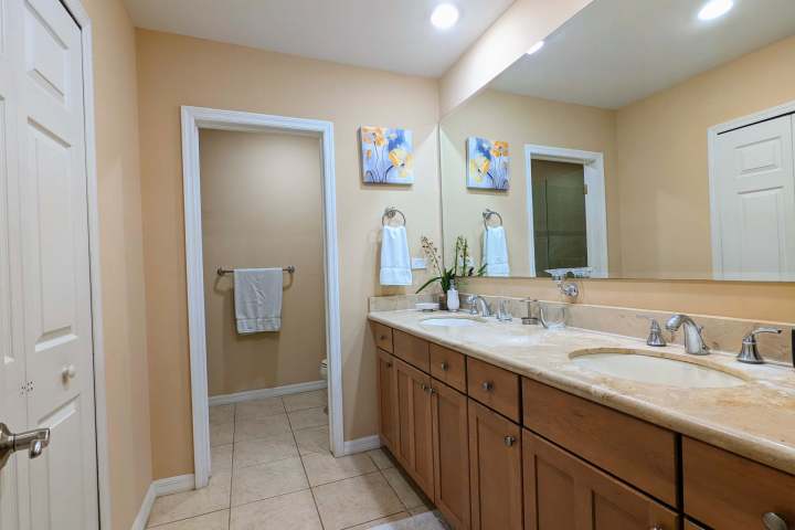 Modern bathroom with double sinks, wood cabinets, and artwork on beige walls.