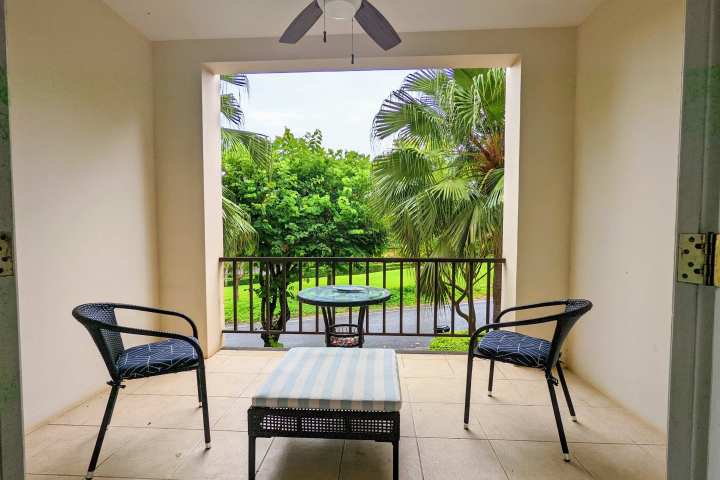 Balcony with two chairs, table, and a view of palm trees.
