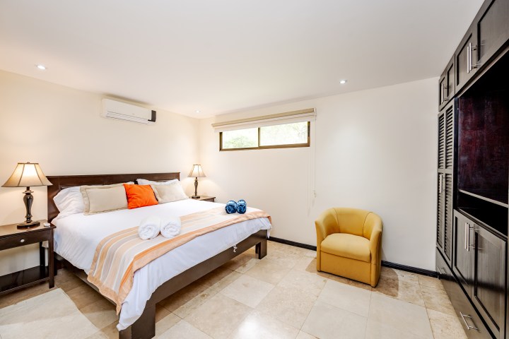 Bedroom with a bed, pillows, two lamps, yellow chair, and wardrobe.