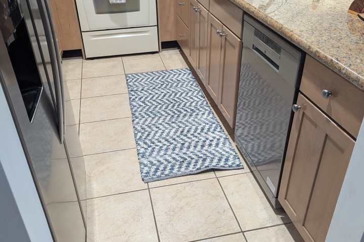 Modern kitchen with beige cabinets, a stove, oven, and a blue geometric rug on tiled floor.