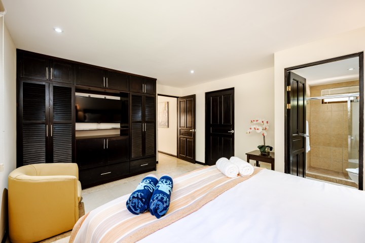 Bedroom with bed, black wardrobe, TV, chair, and open bathroom door.