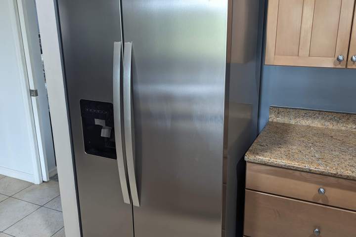 Stainless steel refrigerator in a kitchen with wooden cabinets and granite countertops.