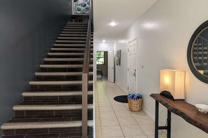 Interior hallway with staircase, table, lamp, and round mirror on beige tiled floor.