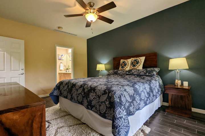 Bedroom with blue accent wall, bed with patterned bedding, ceiling fan, and two lamps on wooden nightstands.