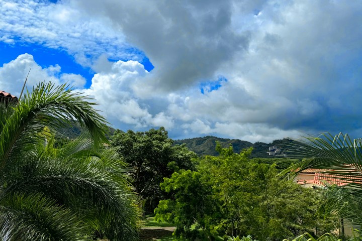 View of lush green trees and hills under a cloudy sky with patches of blue.