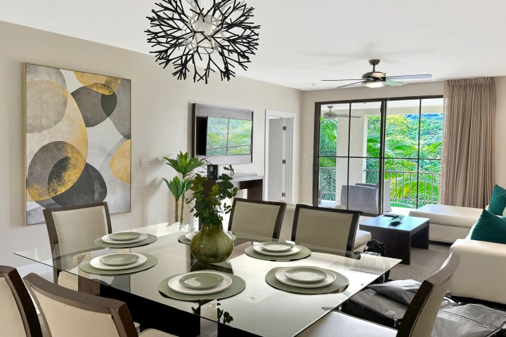 Modern dining and living area with glass table, art, chandelier, and balcony view.