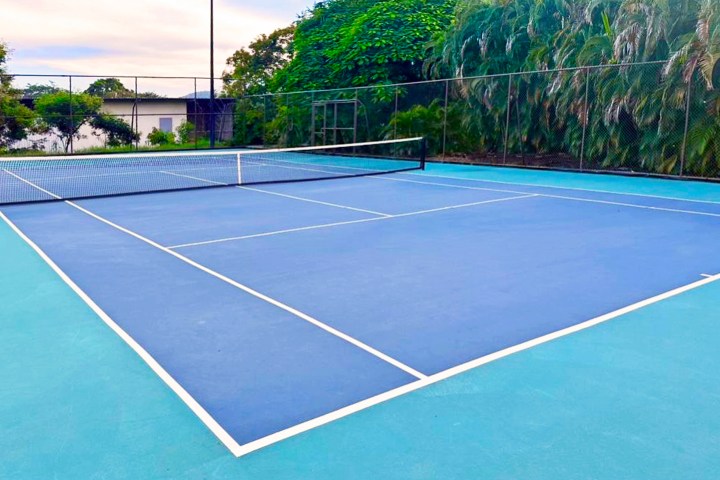 Outdoor tennis court with blue surface and surrounding greenery.