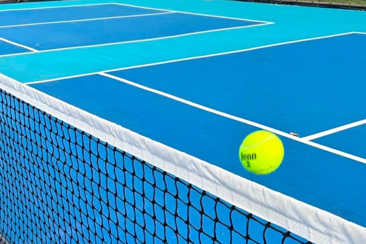 Tennis ball in motion above a blue court with a white net in view.