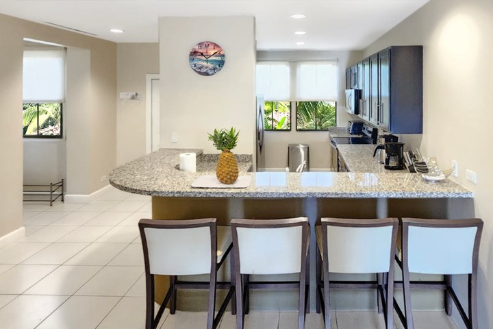 Modern kitchen with bar seating, granite countertop, and fruit decoration.