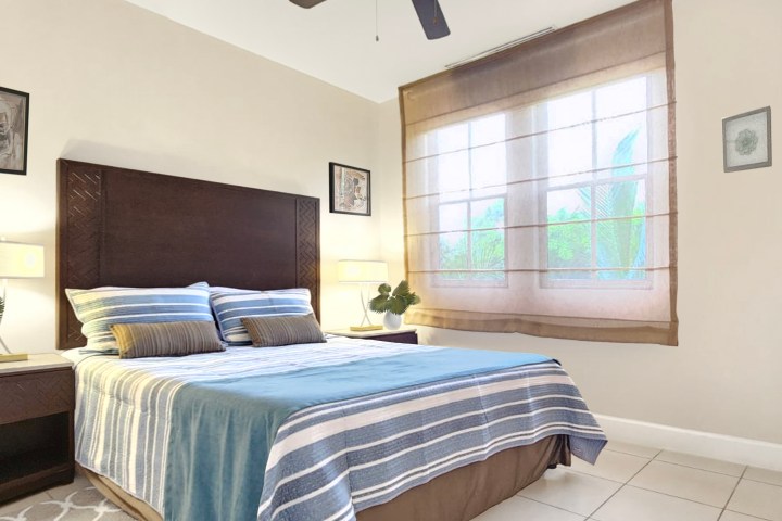 Cozy bedroom with a striped bedspread, nightstands, plants, and framed art on walls.