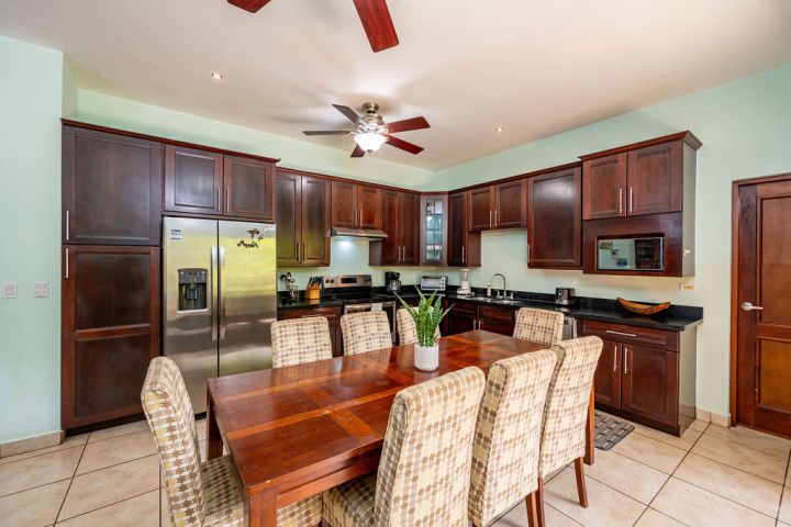 Modern kitchen with wooden cabinets, dining table, and stainless steel fridge under a ceiling fan.