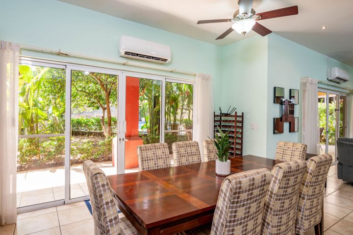Dining room with checkered chairs, table, plant, glass doors, view of garden, and ceiling fan.