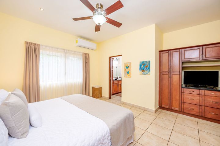 Bedroom with bed, ceiling fan, TV, wooden cabinets, and bathroom entrance.