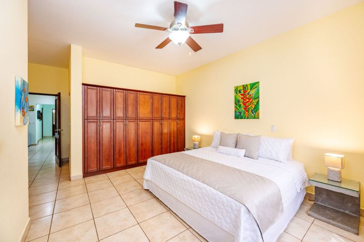 Bedroom with a large bed, wooden wardrobe, ceiling fan, and yellow walls.