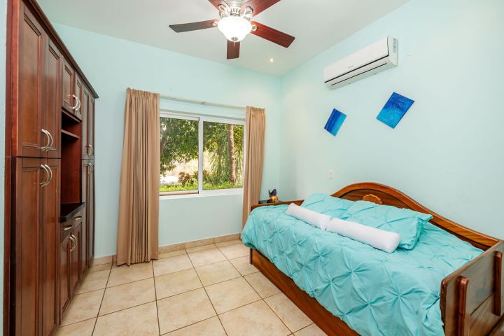 Bedroom with blue walls, wooden bed, ceiling fan, large window, and wooden cabinet.