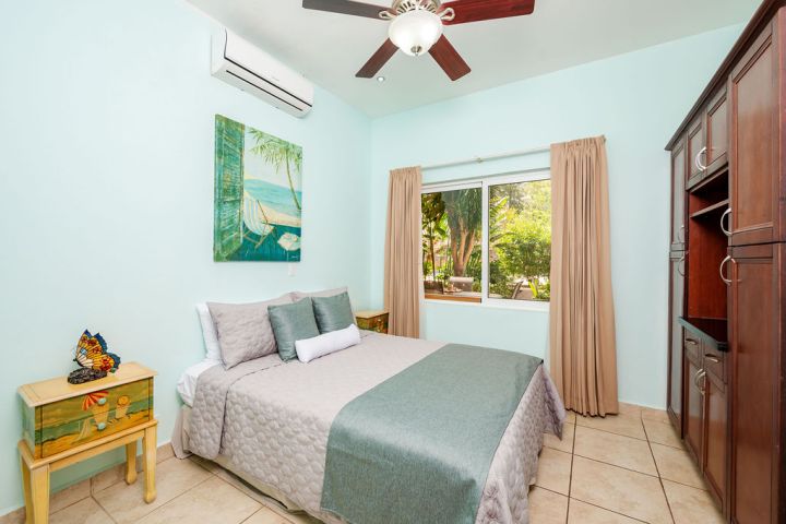 Bedroom with bed, light blue walls, painting, and large window opening to a garden view.