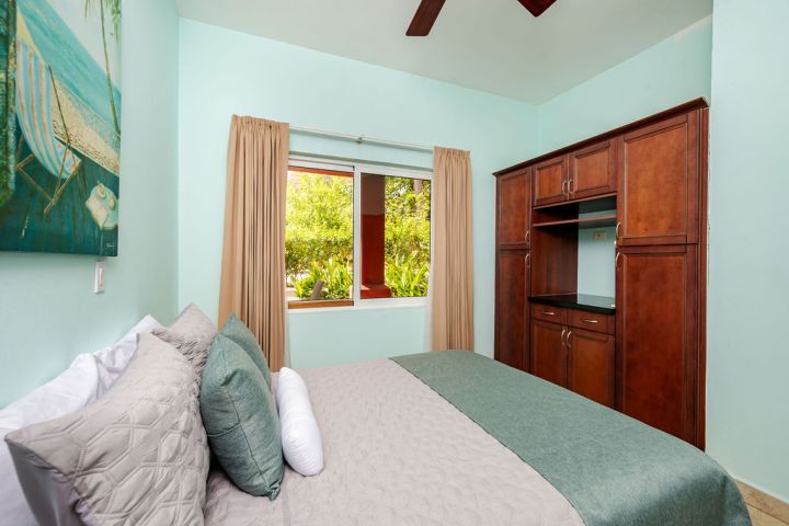 Bedroom with a bed, light blue walls, window view of greenery, and a wooden wardrobe.