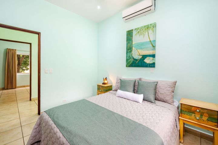Bedroom with a double bed, teal bedding, and beach painting on a mint green wall.