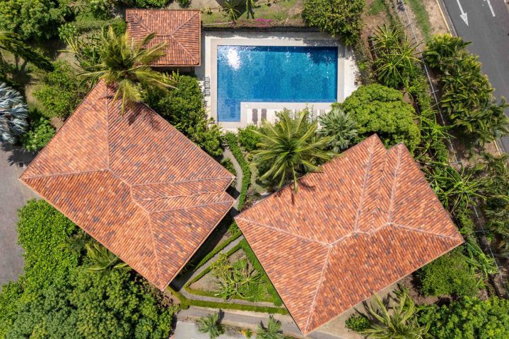 Aerial view of houses with red-tiled roofs and a rectangular pool surrounded by greenery.