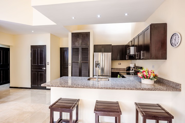 Modern kitchen with granite countertops, dark wood cabinets, bar stools, and stainless steel appliances.