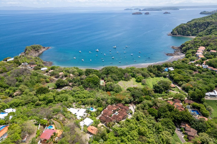 Aerial view of a coastal village with boats in a bay and lush greenery.