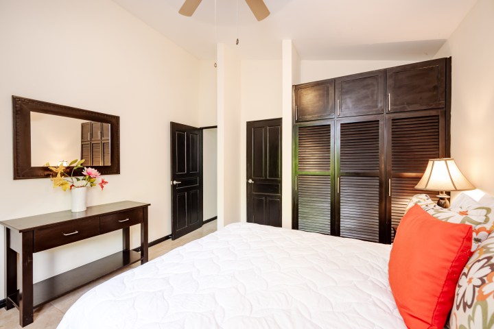 Bedroom with bed, red pillows, dark wood furniture, mirror, and closet doors.