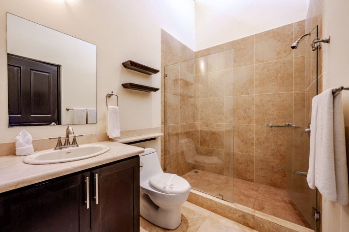Modern bathroom with beige tiles, glass shower, white toilet, sink, and mirror.