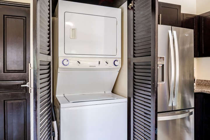 Stacked washer and dryer in a closet next to a stainless steel fridge.