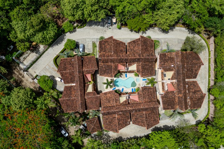 Aerial view of a resort with brown roofs and a central pool surrounded by lush green trees.