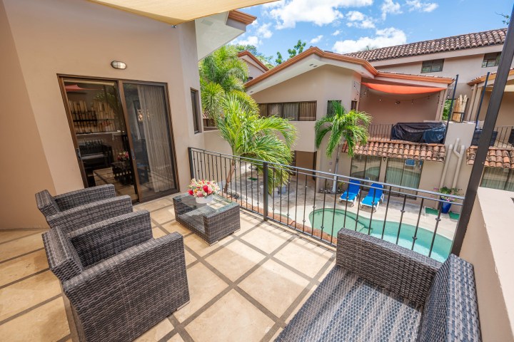 Terrace with wicker furniture overlooking a courtyard pool and adjacent buildings.