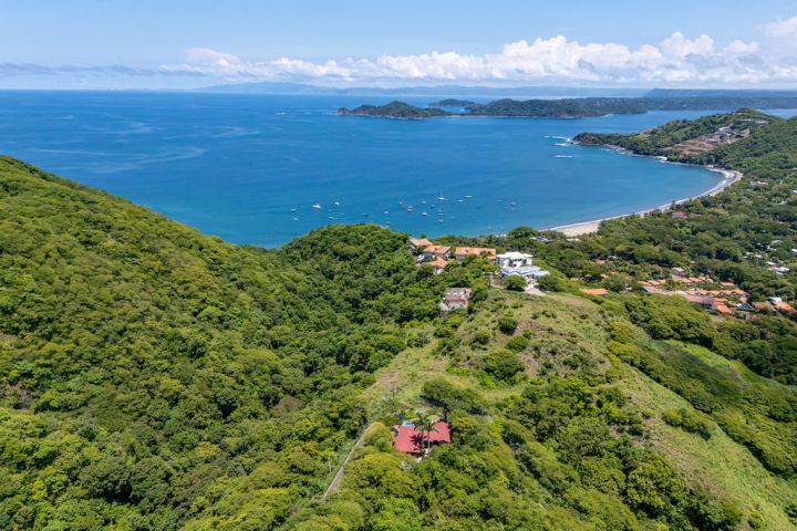 Aerial view of a lush green coastline with a bay and boats on a sunny day.