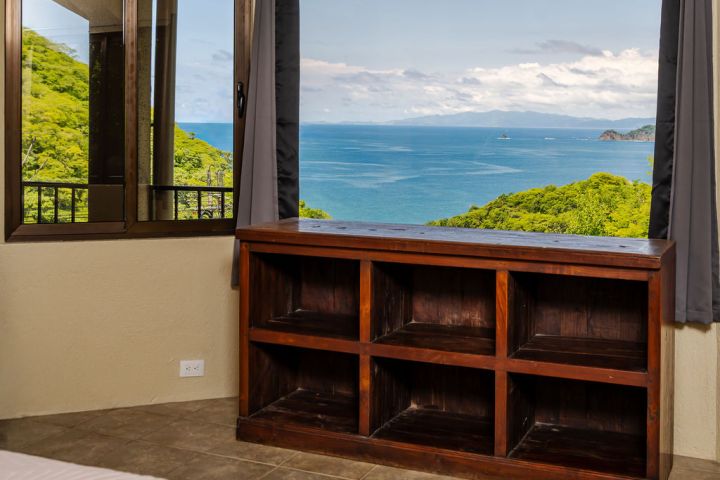 Room with wooden shelves, window view of ocean and green hills.