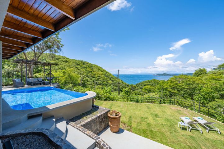 Infinity pool with ocean and lush hills in the background under a clear blue sky.