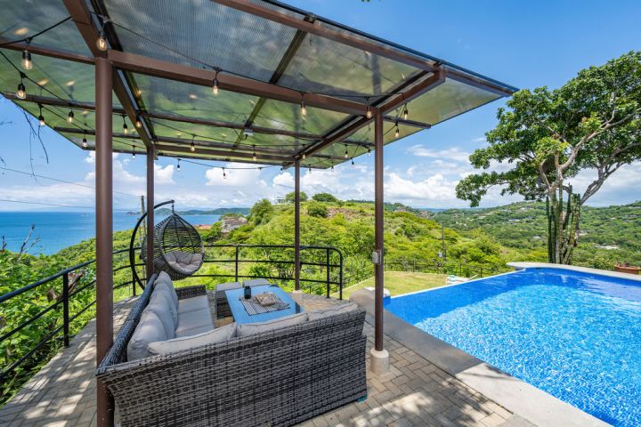 Outdoor lounge with a pool, ocean view, and a hanging chair under a pergola.