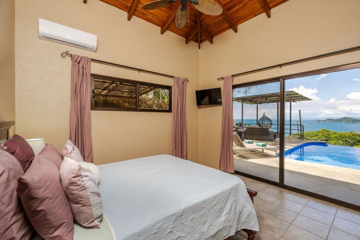 Bedroom with ocean view, large windows, bed, ceiling fan, and pool outside.